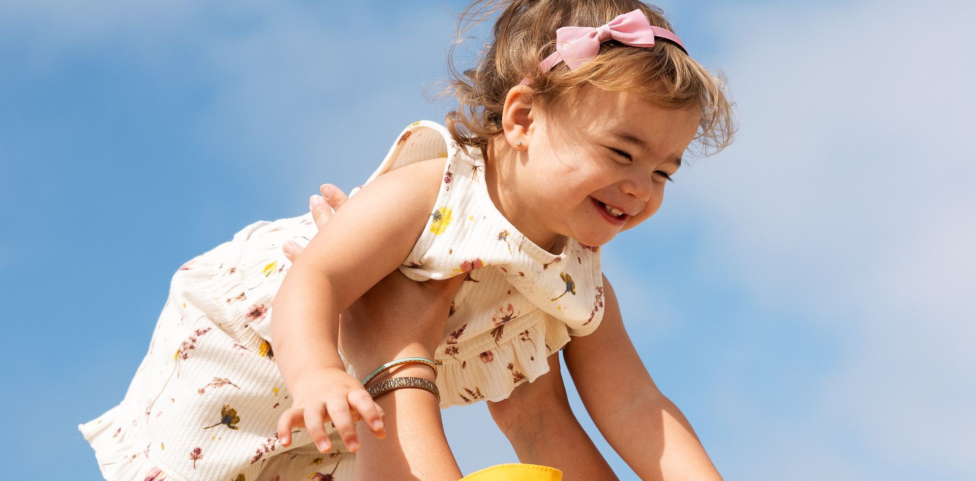 Toddler laughing as she is lifted into a blue sky