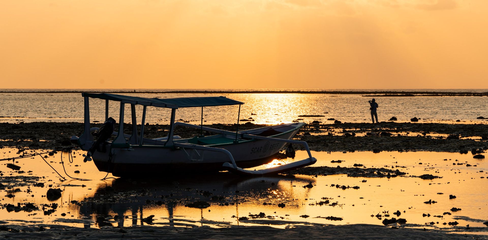 Outrigger boat resting at low tide during a golden sunset in Indonesia