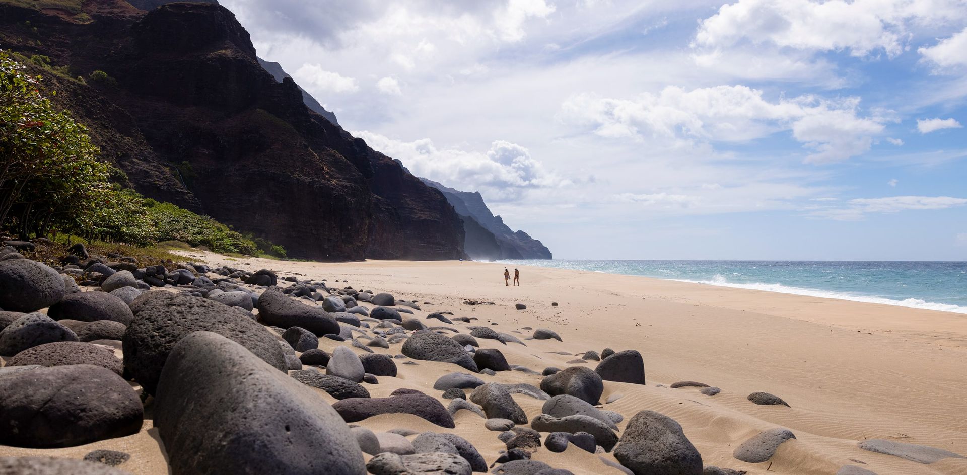 Two hikers on Kalalau Beach below the Na Pali cliffs