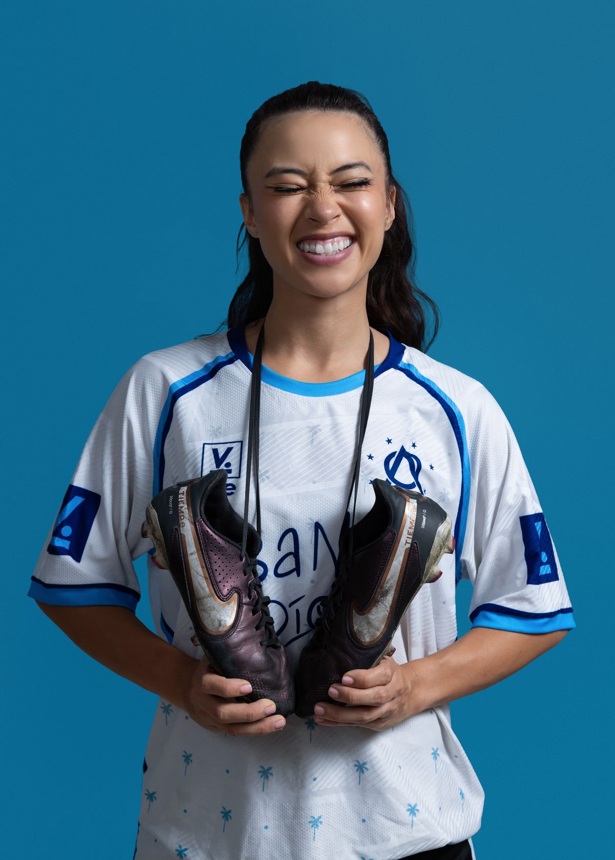 Soccer player smiling with her cleats in the studio